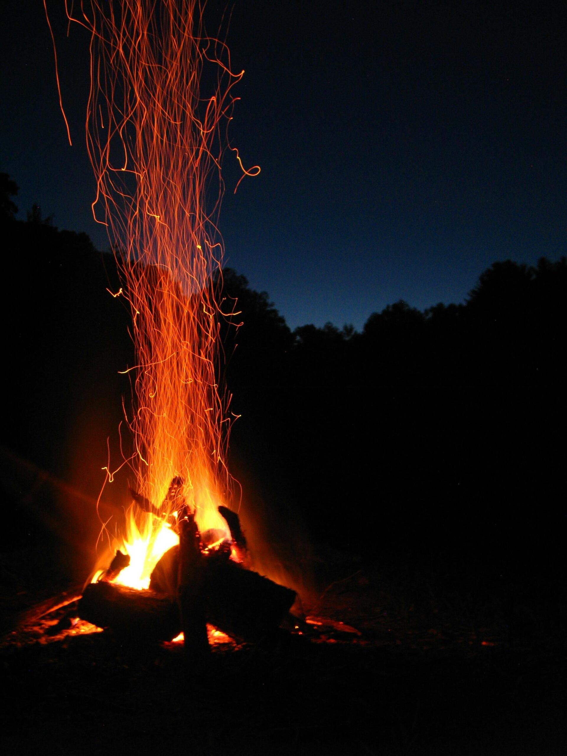 A vibrant campfire with sparks rising against a serene night backdrop, ideal for outdoor themes.