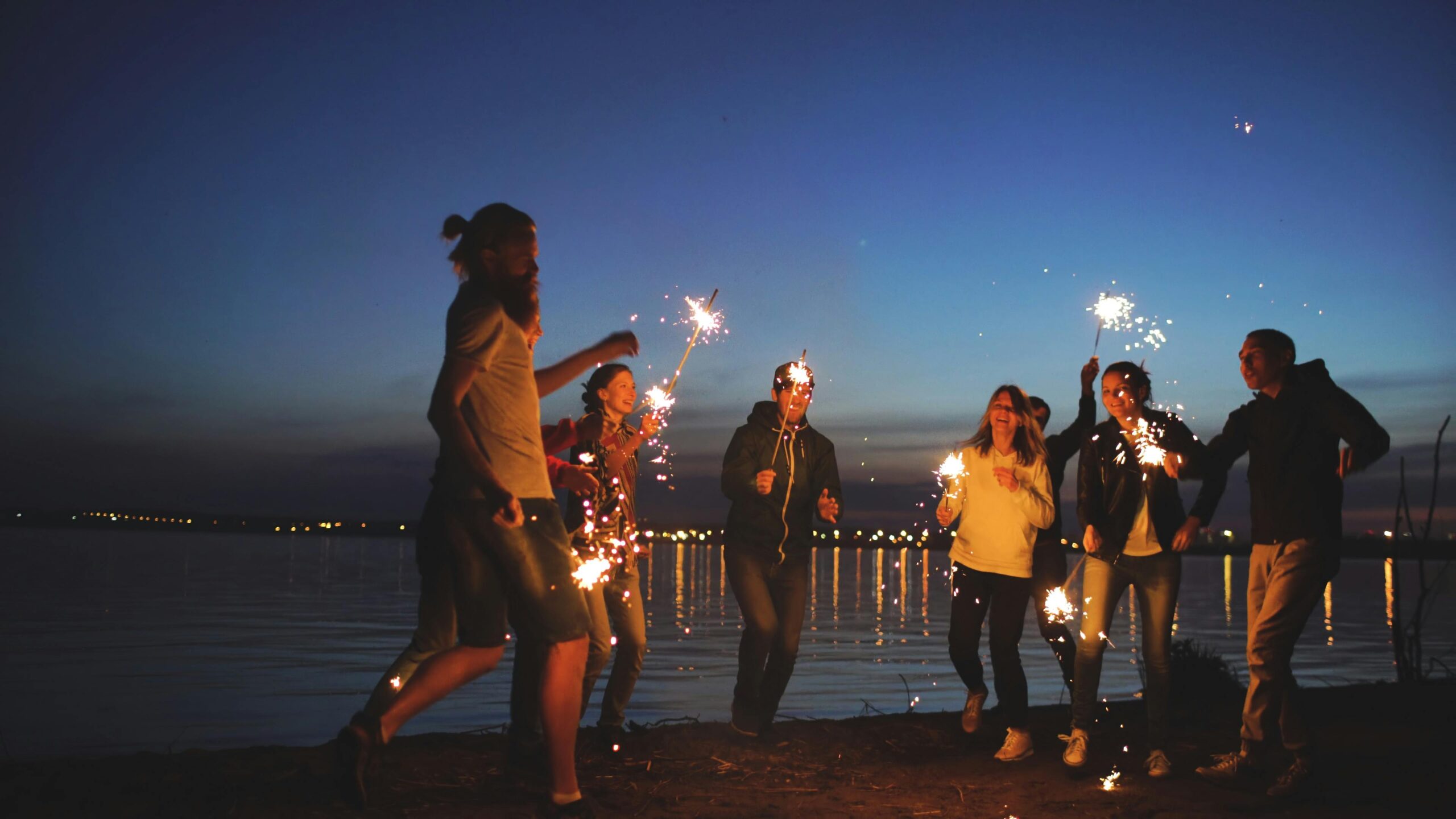 Group of friends enjoying sparklers by the lake at dusk, creating joyful memories.
